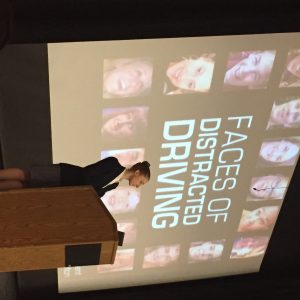 CATA board member Dana Paris at podium in front of faces of distracted driving slide of presentation.